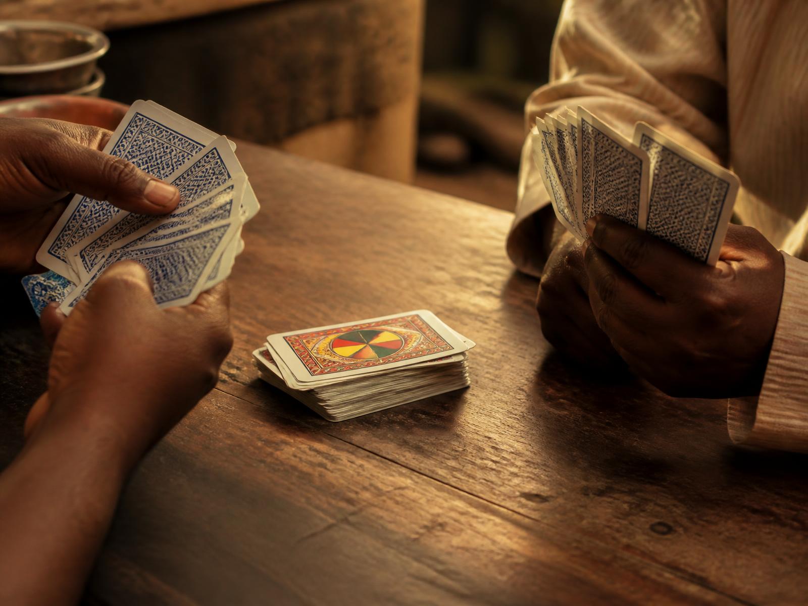 Two players holding fanned WHOT cards across a wooden table